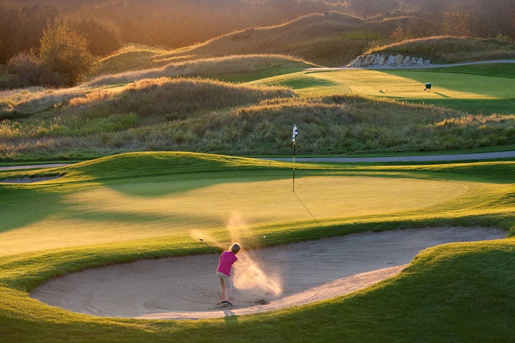 Kvindelig goldspiller er i bunker på golfbaner og slår golfbold og bunkersand fra Dansk Kvarts Industri op i luften