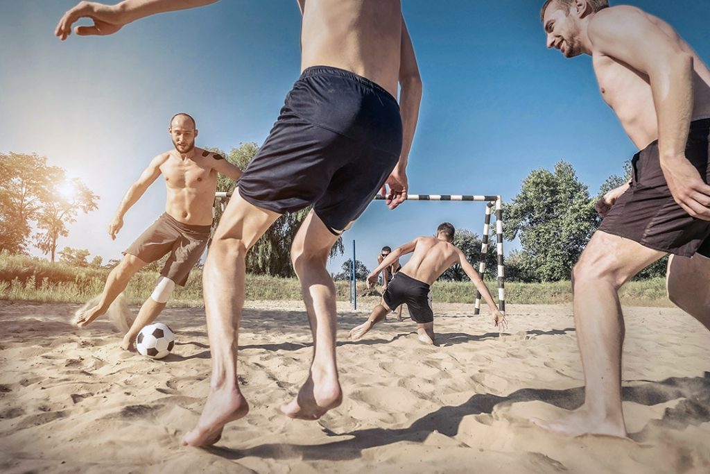 Fem mænd spiller strandfodbold på strandfodboldbane i park med sand til strandfodboldbaner fra Dansk Kvarts Industri